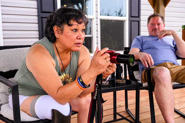 Eileen takes a picture of a bird from her back deck in Theodosia, Missouri, with her husband, Robert, sitting next to her.