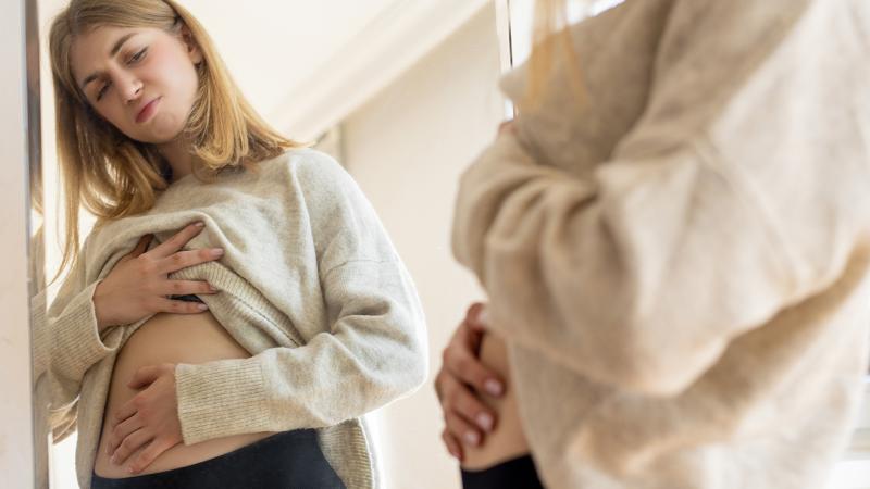 A woman looking at her stomach in the mirror.