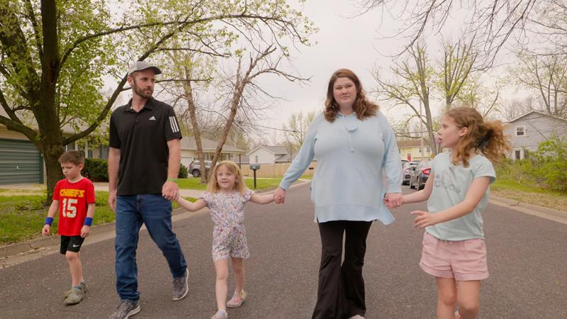 A family of five walking down the street holding hands.