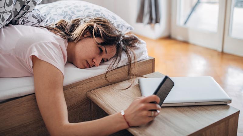 A woman lying in bed, looking at her phone.