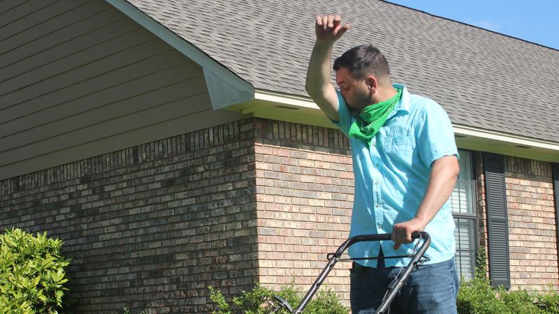 A man sneezing while mowing the lawn.