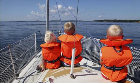 Three children sitting in the front of a sailboat wearing life jackets.