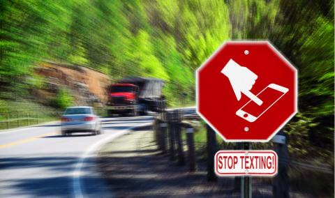 Stop sign with a symbol of a handheld device and the words Stop Texting printed on it. Image is blurred to imply motion and distraction. Symbol is artist own conceptual design.