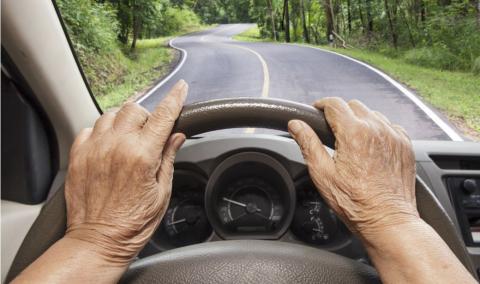 Senior woman driving a car on highway in forest.