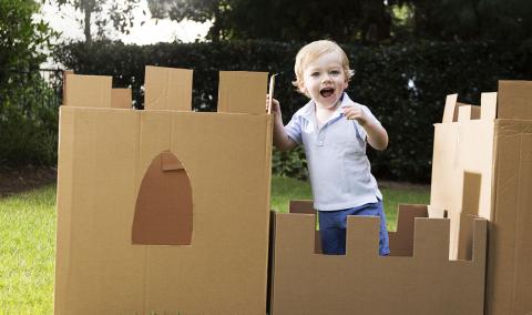 young boy plays in the yard with a castle made from cardboard box