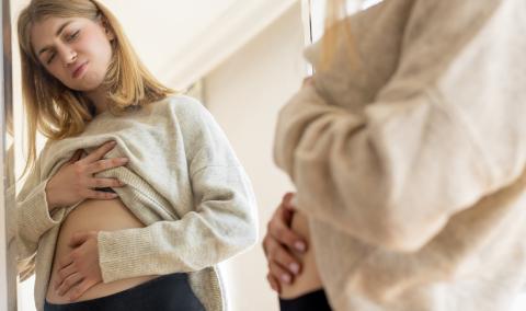 A woman looking at her stomach in the mirror.