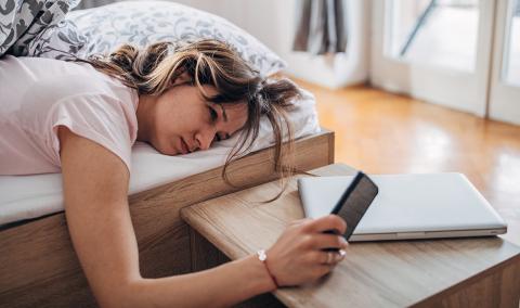 A woman lying in bed, looking at her phone.