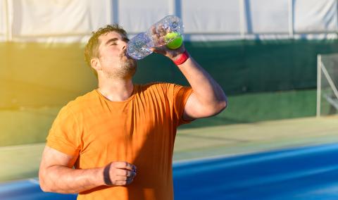 A man drinking a beverage after exercising outdoors.