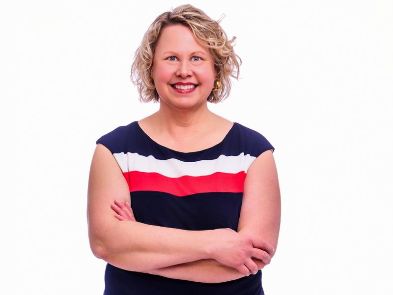 A photo of a woman, smiling with her arms crossed.