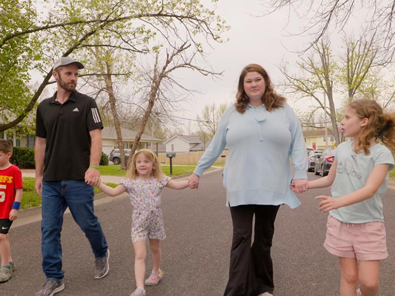 A family of five walking down the street holding hands.