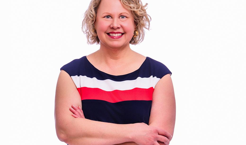 A photo of a woman, smiling with her arms crossed.