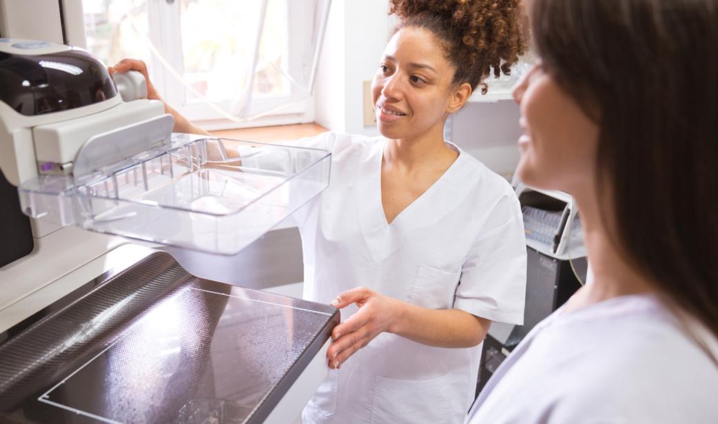 A picture of two women in front of a mammogram machine.
