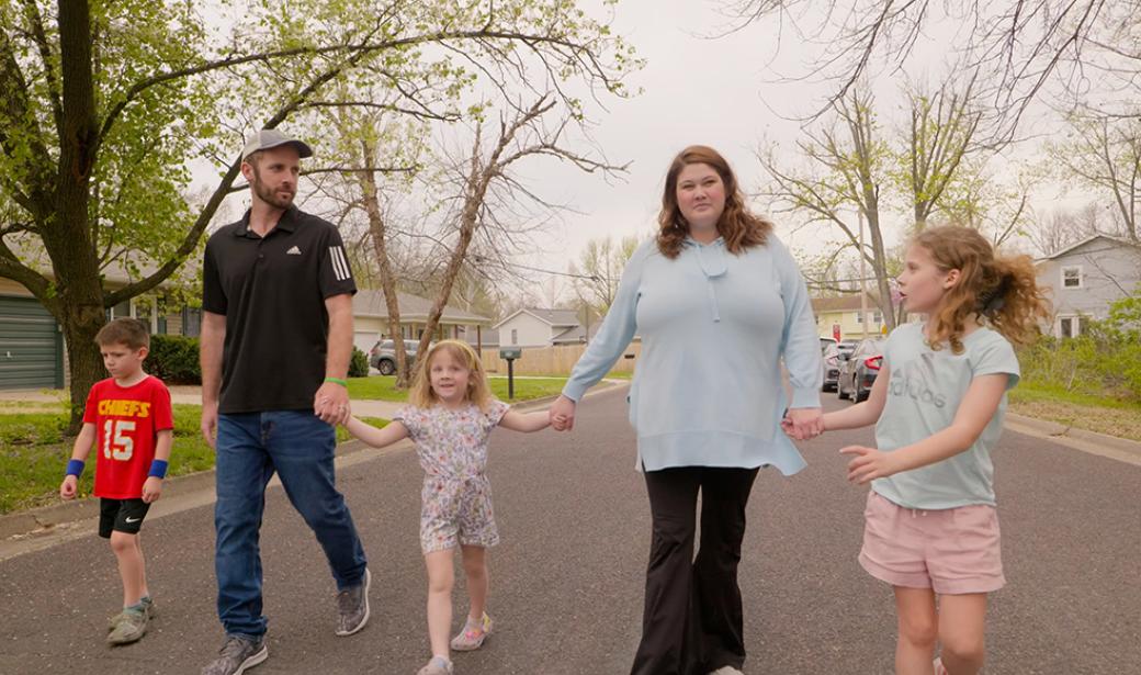 A family of five walking down the street holding hands.