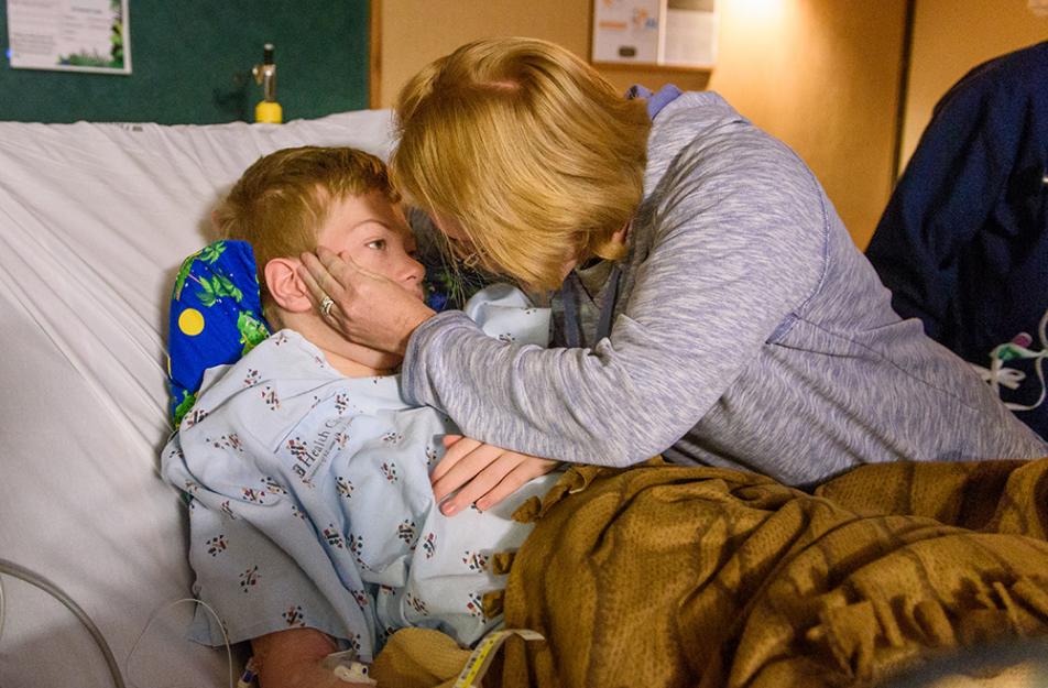 boy in hospital bed hugged by mother