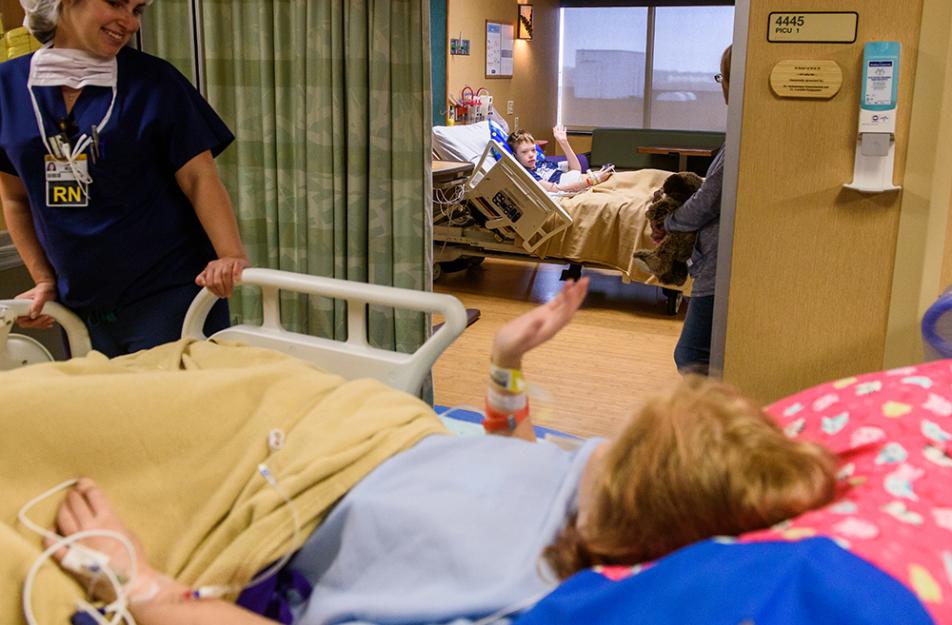 child in hospital bed waves at nurse